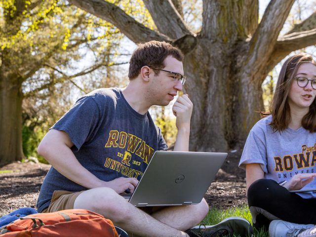 A male and female student sit under a tree at Rowan University studying.