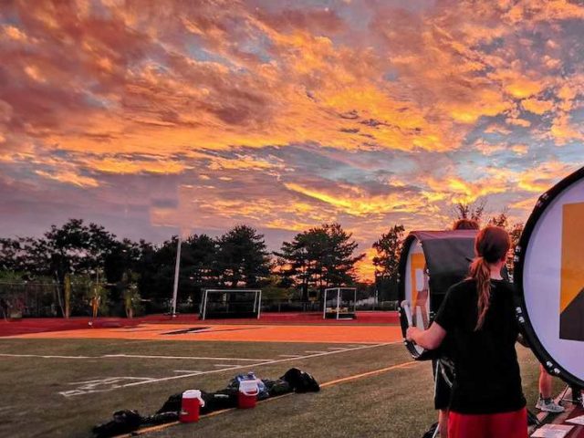 A close up of the R for Rowan on a marching band drum with a dramatic orange sunset behind the drum, at the Rowan University athletic field.