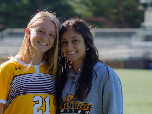 Emily stands close to a friend outside on the soccer field.