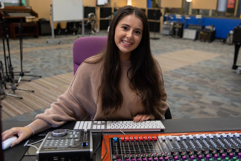 Alyssa smiles sitting at a sound board.