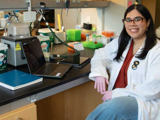 Yesenia sits at a lab table for a portrait.