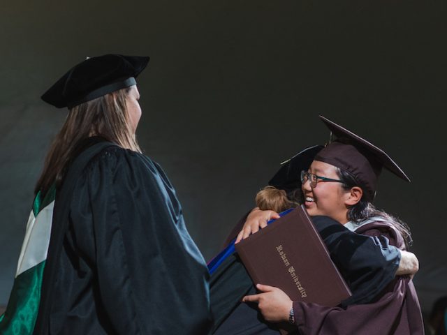 Rowan University graduates cross the stage at graduation, hugging faculty and smiling.