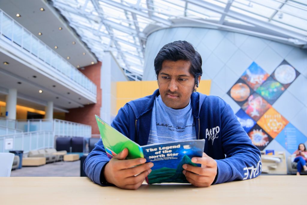 Pavan Goud Juluri looking at a magazine, sitting outside of the Edelmann Planetarium