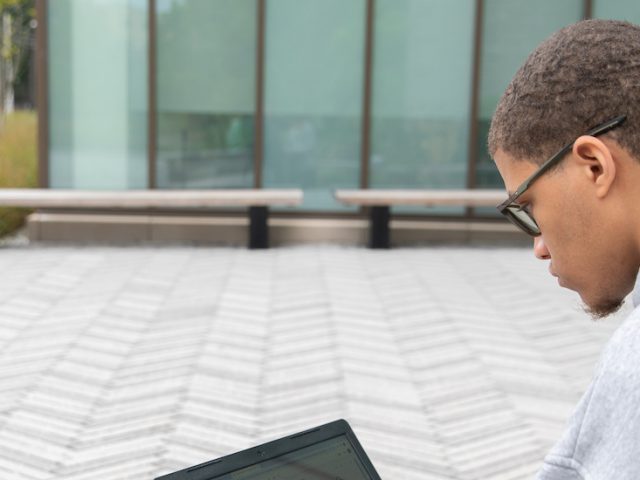 Rowan University computer science major Steven Warner sitting outside of Discovery Hall with his laptop