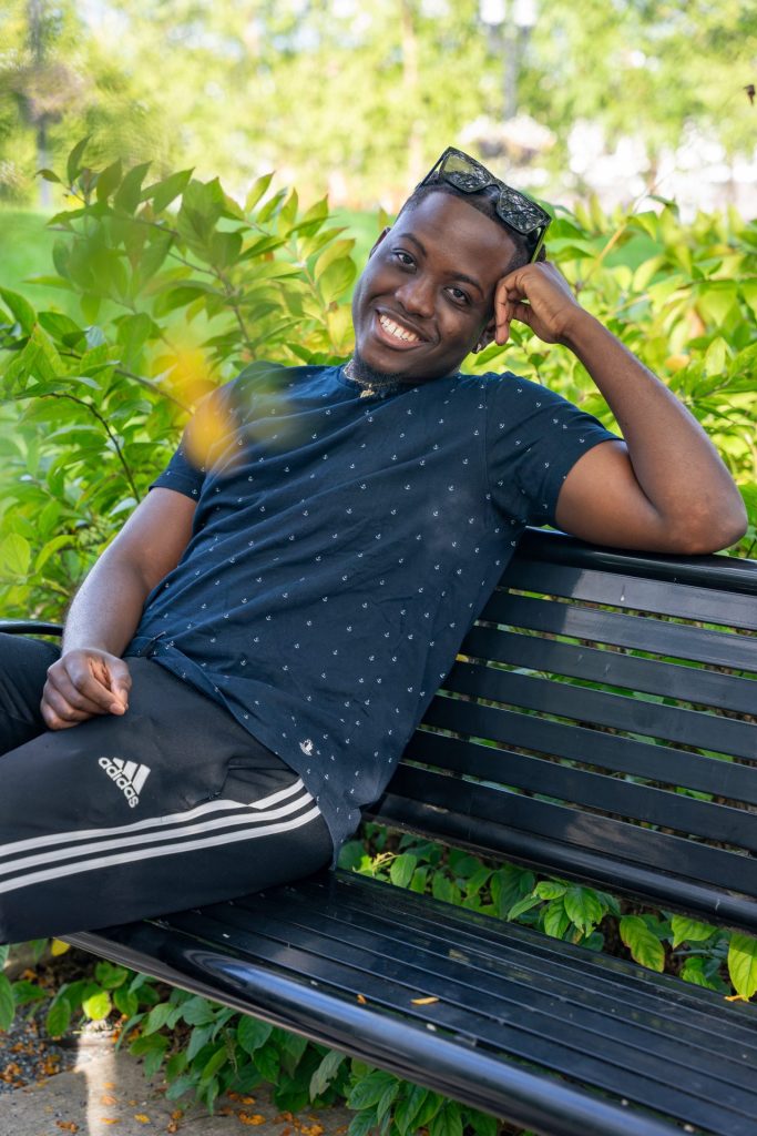 Samuel Poku sitting on a bench outside surrounded by greenery.