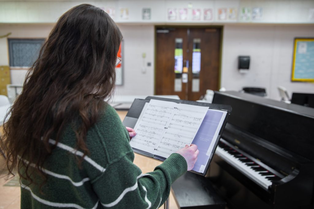 Hannah Potratz looking at her song binder. She is wearing a green and white striped sweater.