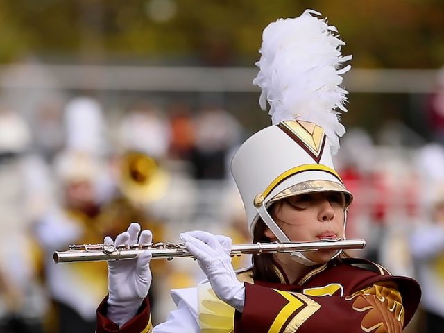 A close up of marching band members in uniform playing instruments duirng a game.