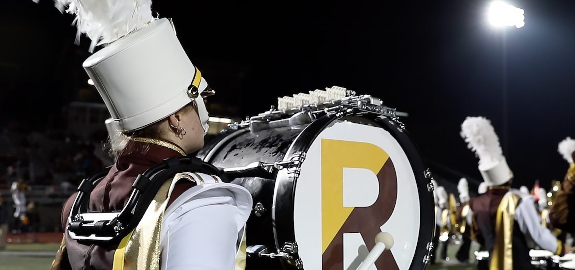 A close up of a Rowan University drum major, showing the large R on the side of the drum and a tall white hat.