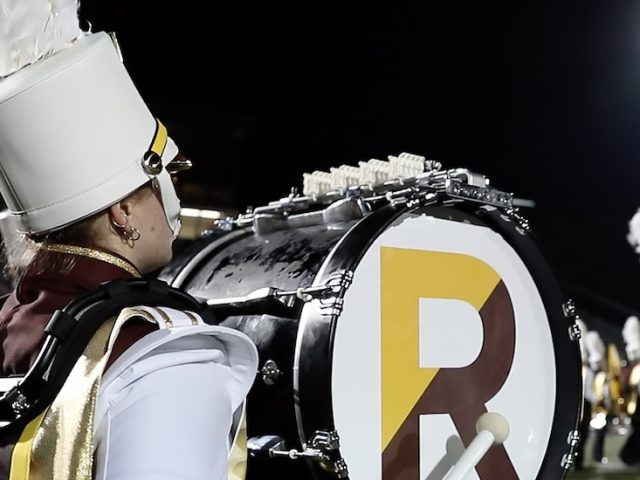 A close up of a Rowan University drum major, showing the large R on the side of the drum and a tall white hat.