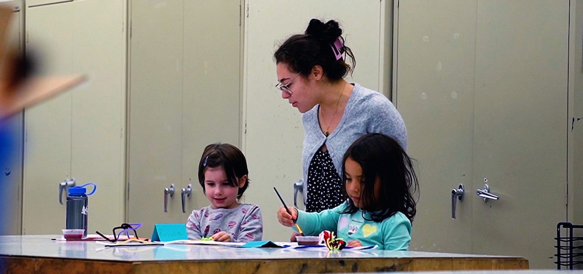 A Rowan University Art Education major working with two students on an art project through the smART program.