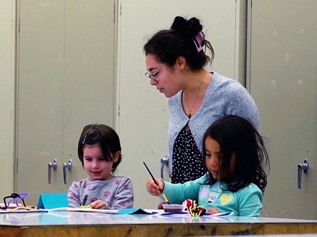 A Rowan University Art Education major working with two students on an art project through the smART program.