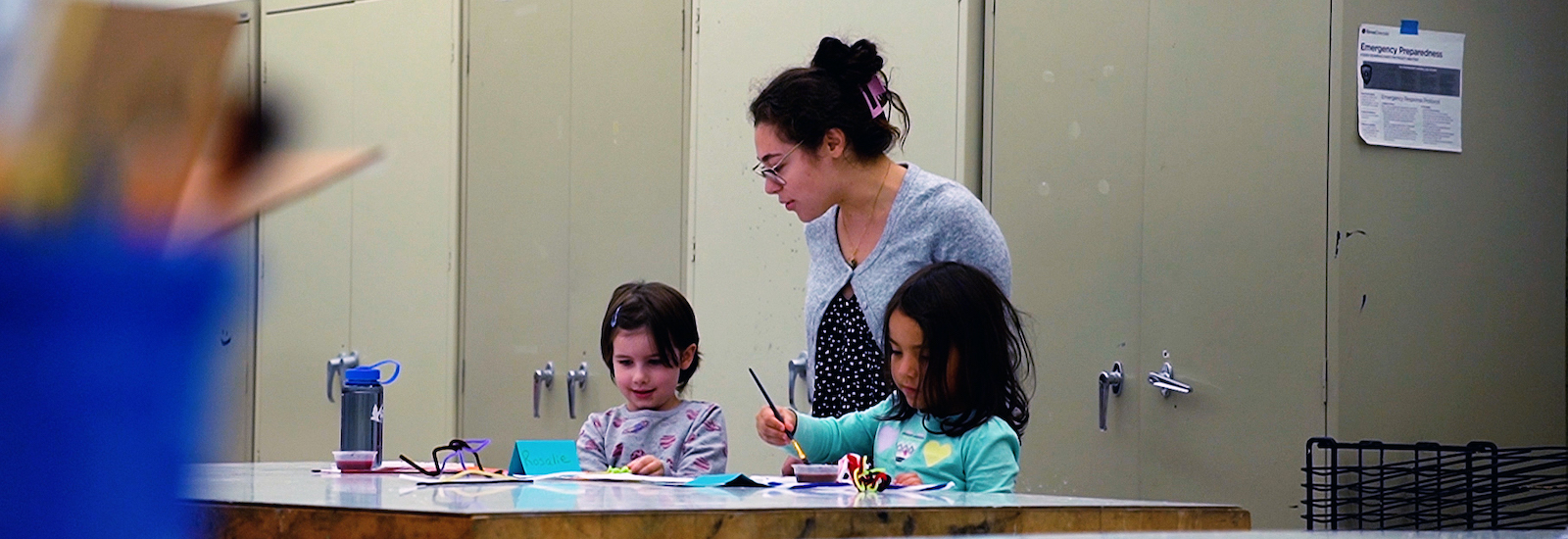 A Rowan University Art Education major working with two students on an art project through the smART program.