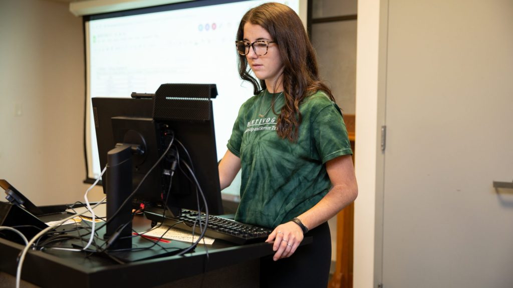 Jordyn working on a laptop inside of an Honors classroom.