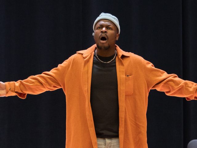 Vocal performance major Moses at Rowan University singing on the Boyd Concert Hall stage. He is seen with his arms out.