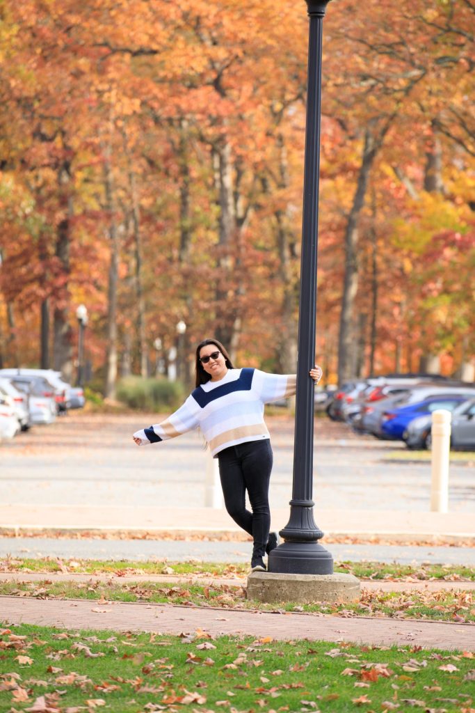 Suzie holding onto a lamp post on Rowan University's campus. She is pictured in a sweater and leggings. 