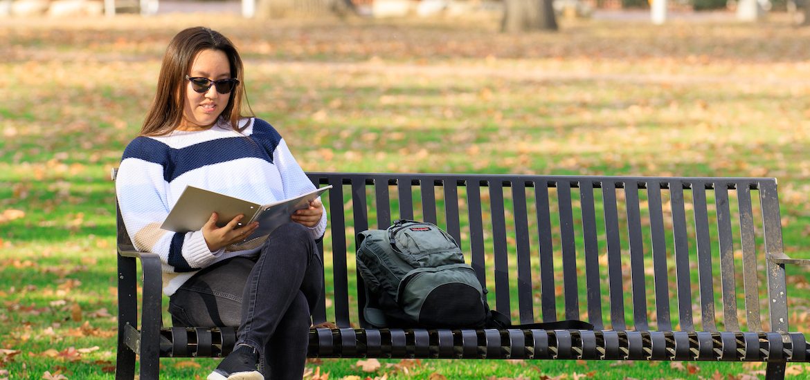 Suzie sits on a bench at Rowan University's campus, reading a book.