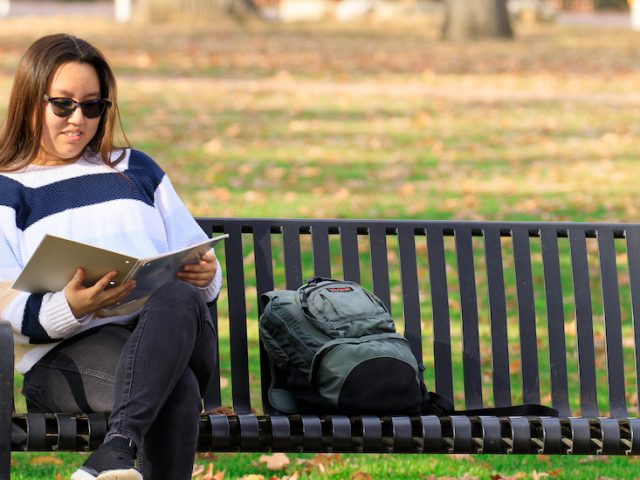 Suzie sits on a bench at Rowan University's campus, reading a book.