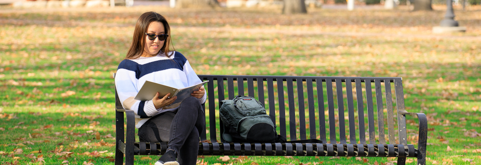 Suzie sits on a bench at Rowan University's campus, reading a book.