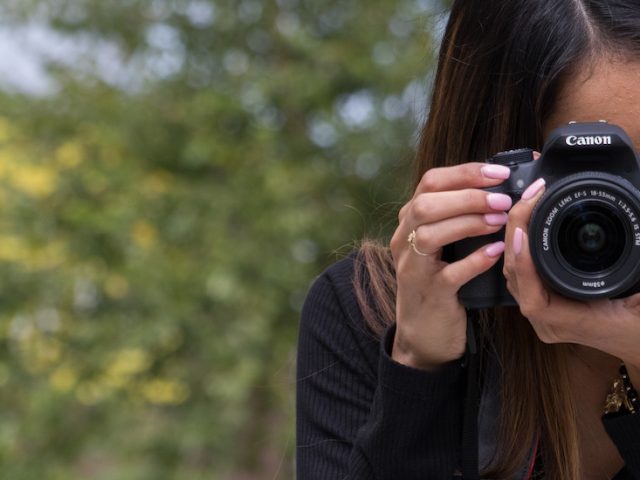 Student stands holding a DSLR camera, taking a photo.