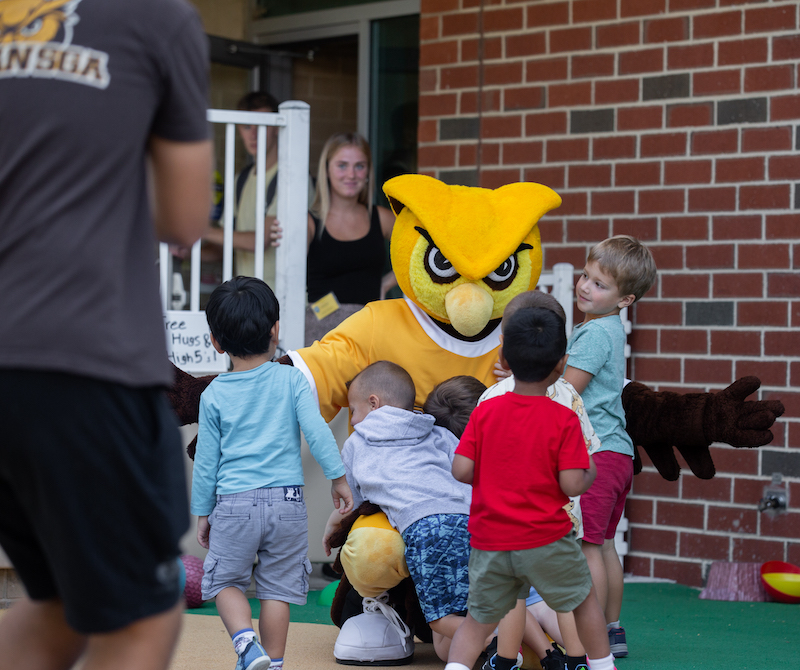 The university mascot crouches to hug children crowding him at the Rowan Preschool.