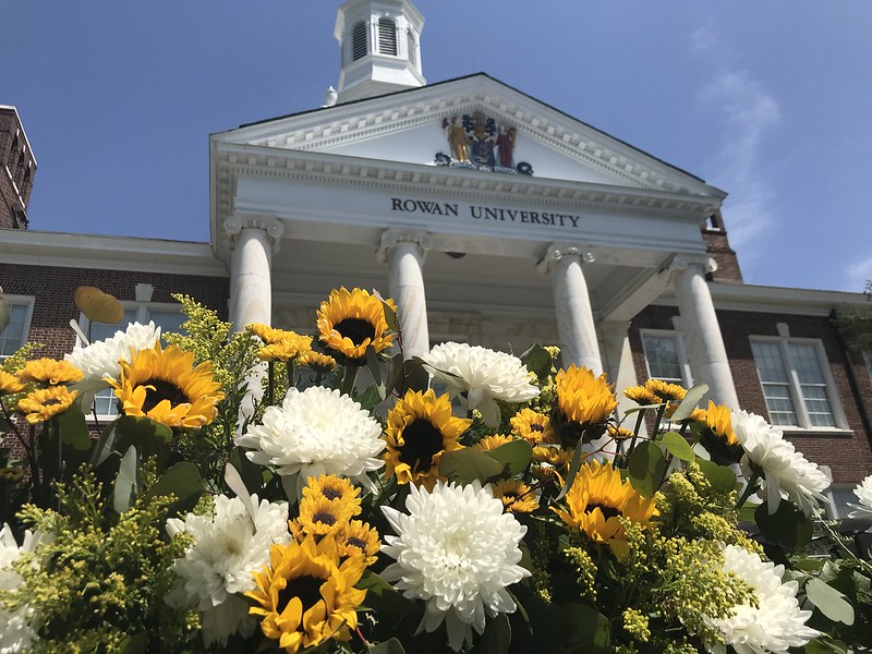 A view from the ground, looking up at yellow and brown flowers adoring the front of Bunce Hall at graduation. 