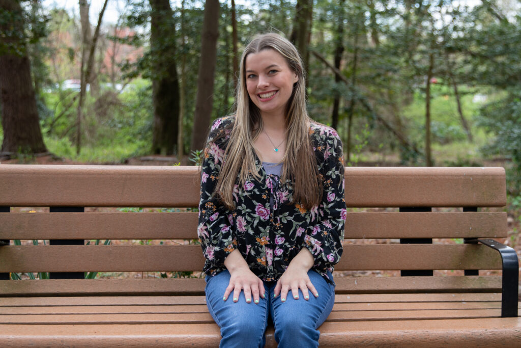 Lauren sitting outside on a bench at Rowan. She is seen wearing jeans and a black floral top.