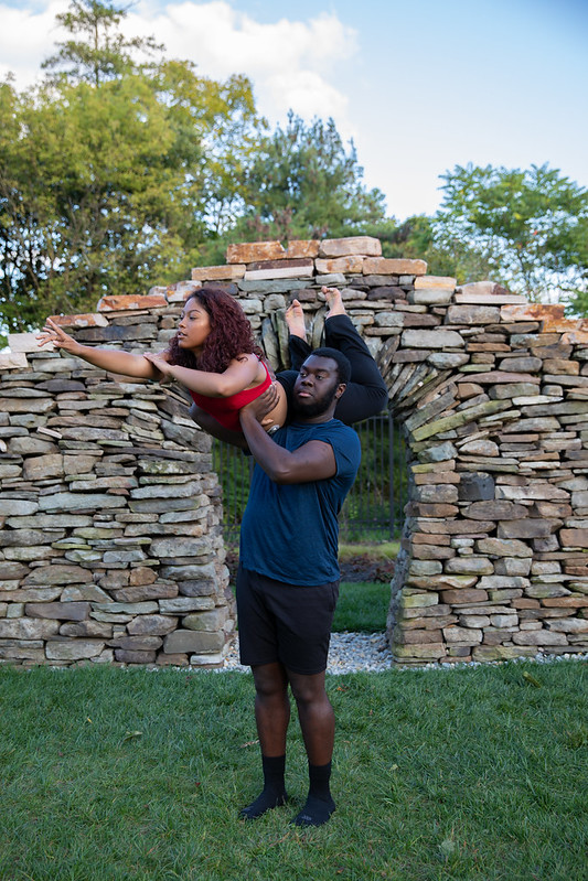 A Rowan dancer holds up and supports a second dancer on their shoulder, as the lifted dancer holds a pose with legs and arms outward. 