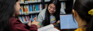 Three students huddle together, heads down, to study.