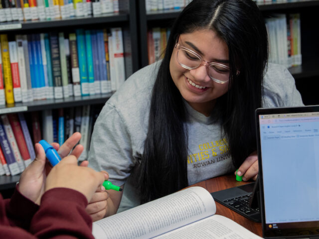 Three students huddle together, heads down, to study.