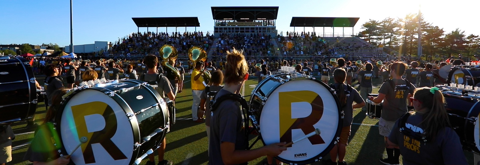 A side view of drum majors playing a drum during marching band, with a giant R on the side of the drum for Rowan.