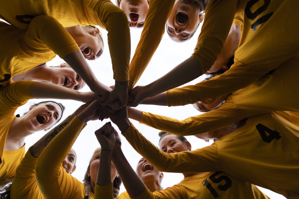 A view up, from the middle of a sports team huddle where everyone put their hands in the center, creating a starbust pattern. 