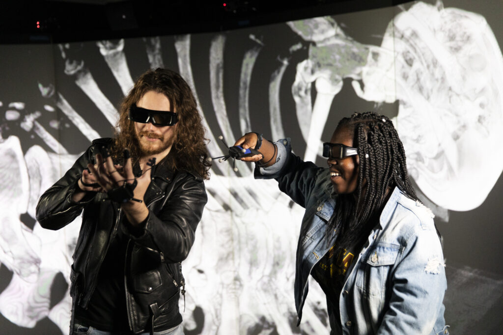 Two students experience the VR lab while examining the image of a skeleton. 