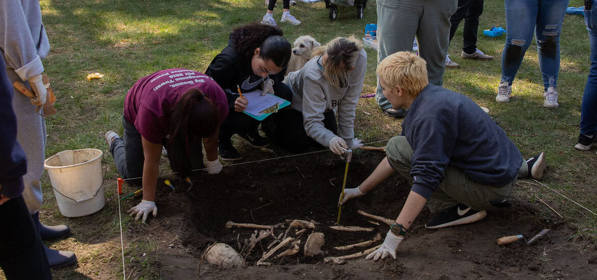 Looking down at three students crouched on the ground, iarchaeologist Burials of a Revolutionary War battle near Rowan University.