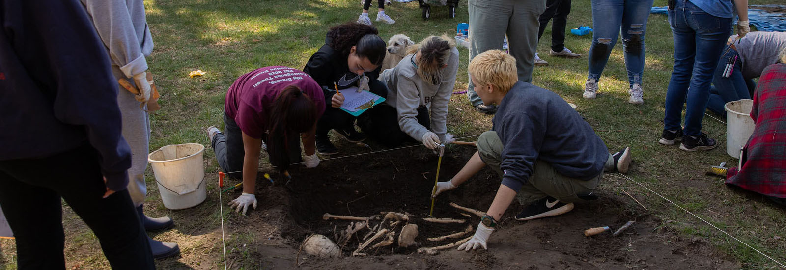 Looking down at three students crouched on the ground, iarchaeologist Burials of a Revolutionary War battle near Rowan University.