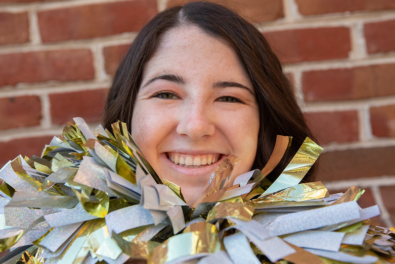 A close up of Jordyn's face as she smiles and holds two glittery pom poms under her chin. 