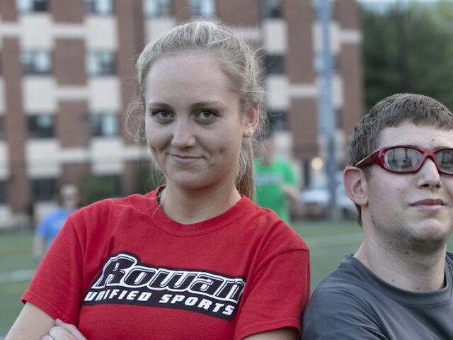 Two students stand shoulder to shoulder on an athletic field at Rowan University.