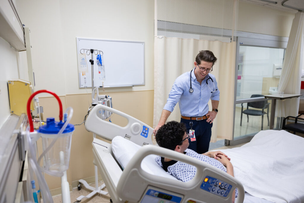 Richie stands casually by a patient's bedside, chatting with them. 