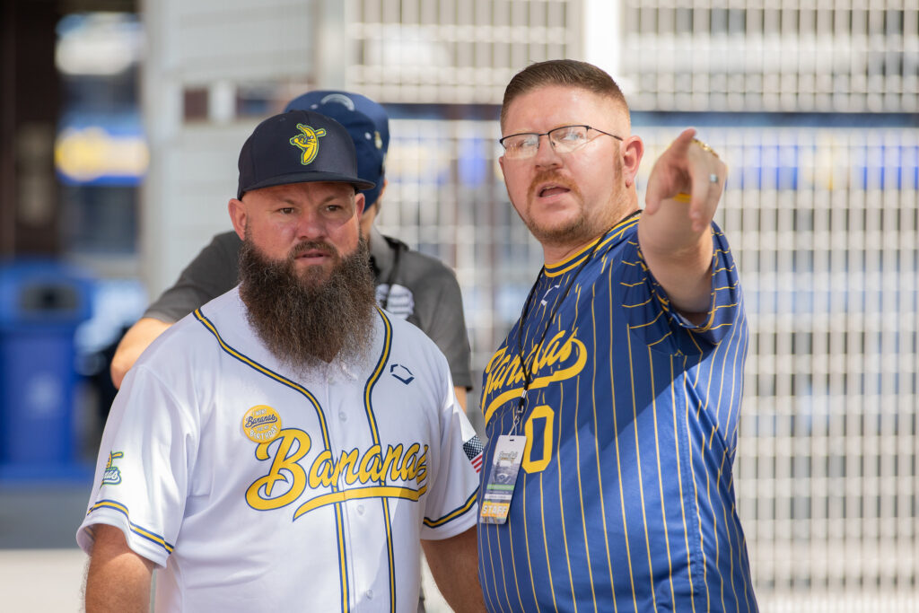 Rowan University alumnus and Savannah Bananas Matt Graifer  point to a stage off screen, standing with Vincent.