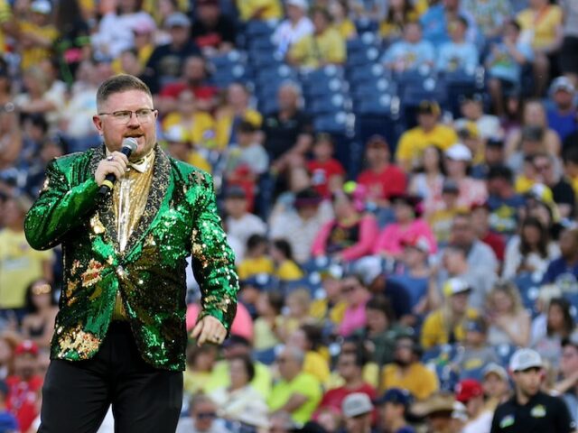 Rowan University alumnus Matt Graifer of the Savannah Bananas wears a green glittery suit jacket and holds a microphone with a stadium full of fans behind him.