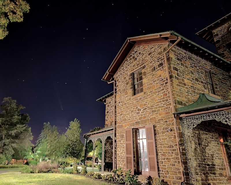 Rowan University's Hollybush Mansion is an example of Victorian, Eastlake, and Renaissance Revival styles and is seen here framed in the foreground, with the dark sky sprinkled with white dots of stars and a faint white streak for the comet. 