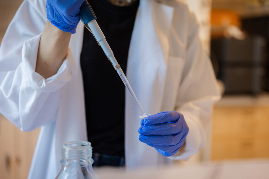 A close up of a purple gloved hand and a Rowan University biomedical engineering student's white lab coat as they use a pipette. 