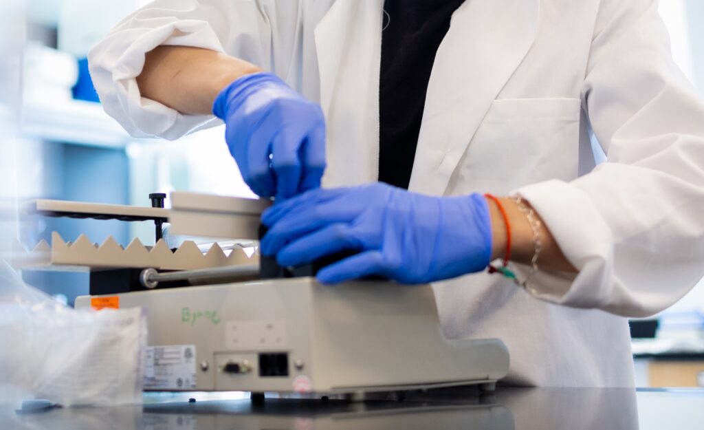 A close up of a purple gloved hand and a Rowan University biomedical engineering student's white lab coat as they use a measurement tool. 