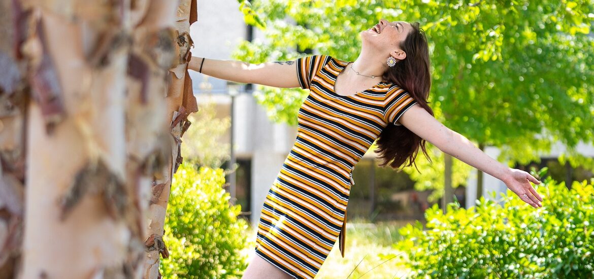 A Rowan University holds onto a tree, leaning backward with one arm hanging freely, laughing.