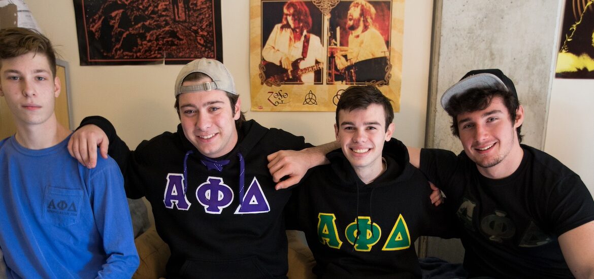 Four students sit in a male dorm room adorned with music posters across the wall.