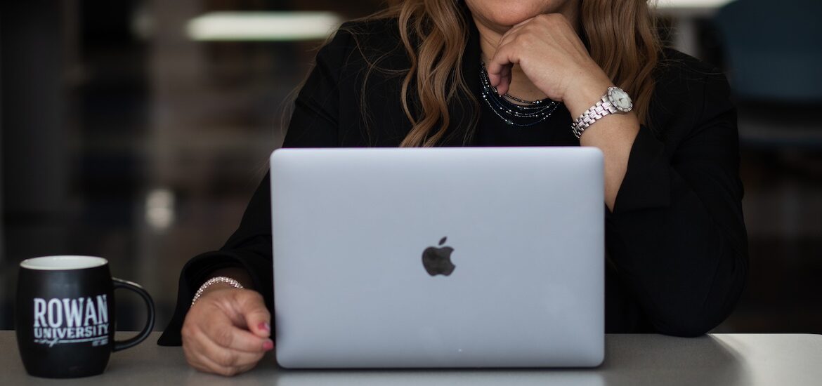 A close up of a professional in a suit working on a laptop, with a Rowan University mug next to them.