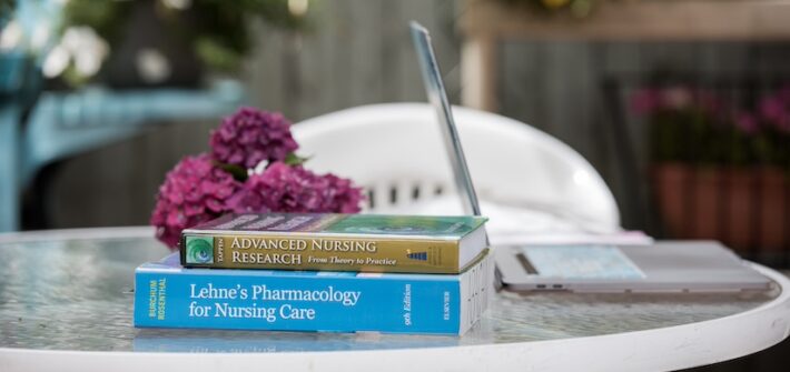 Masters of science in nursing books on an outdoor patio table with a laptop and flowers.