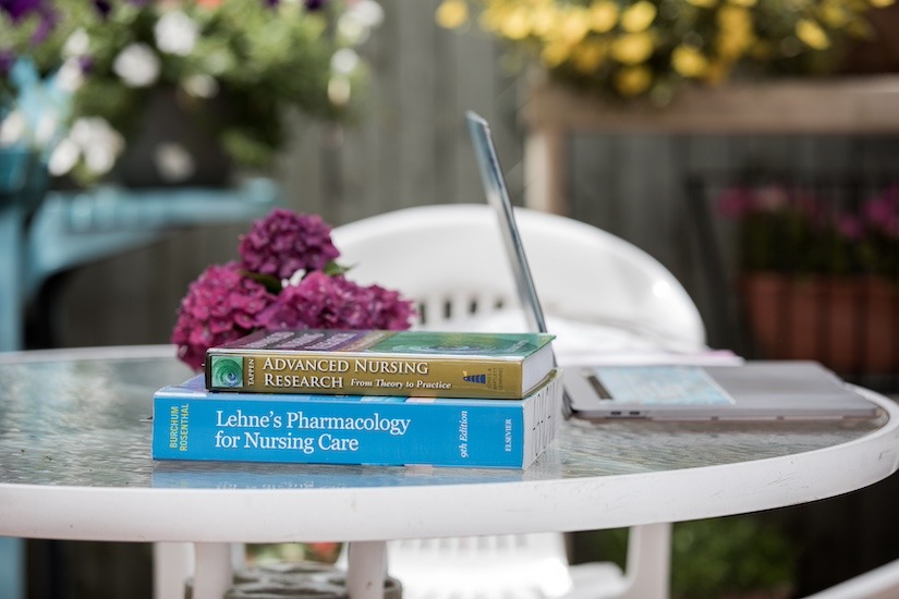 Masters of science in nursing books on an outdoor patio table with a laptop and flowers.