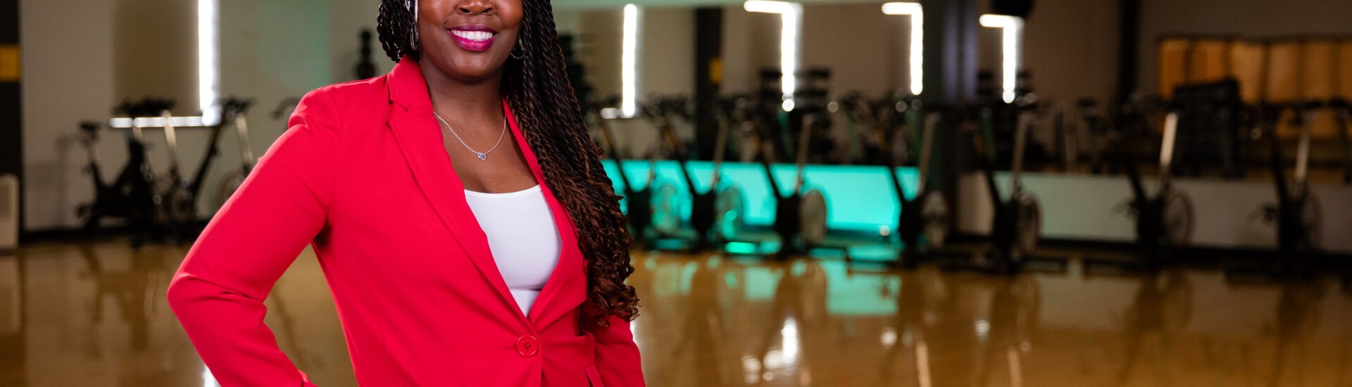 Confident health coach in a red suit standing in a fitness studio.