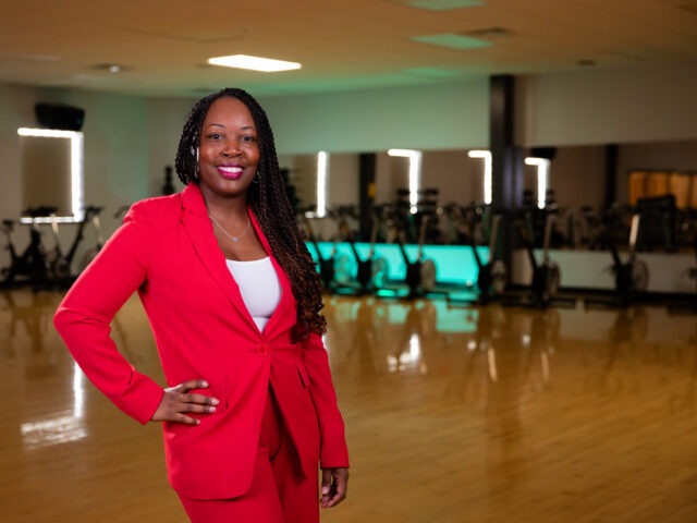 Confident health coach in a red suit standing in a fitness studio