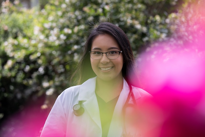 A Rowan University master's in nursing student stands in her backyard, wearing a white coat and a stethoscope around her neck. 